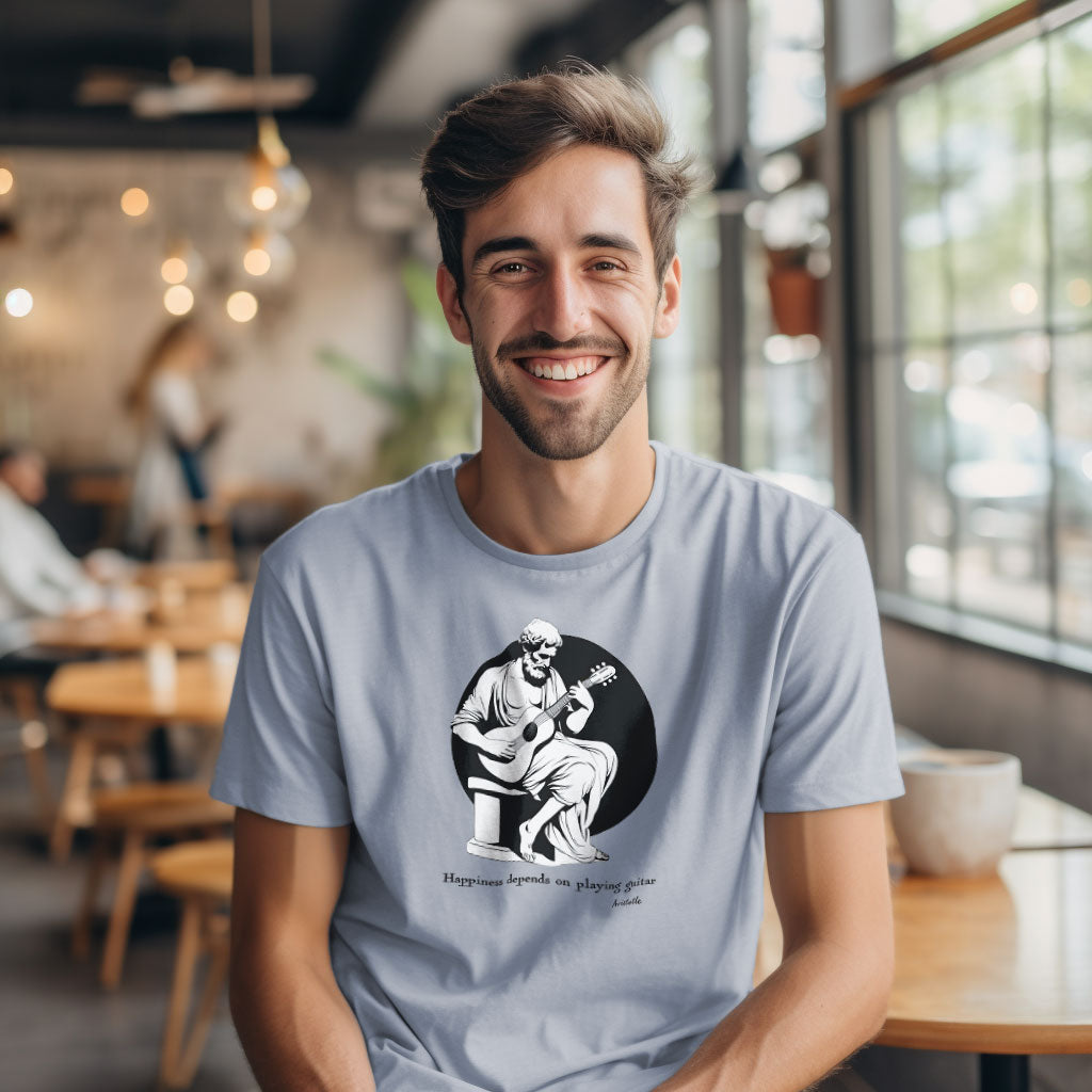 A guy in a cafe wearing a light blue t-shirt with a print of Aristotle playing a guitar and the caption Happiness depends on playing guitar