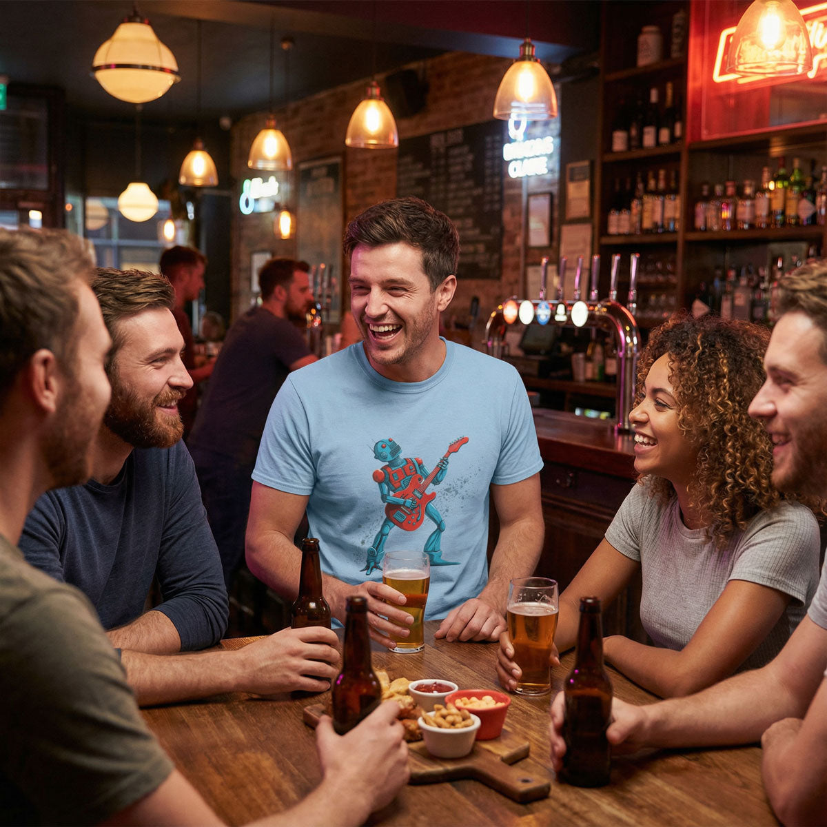 Man sitting with friends in a lively pub, laughing and holding a beer while wearing a light blue T-shirt featuring a cartoon robot playing an electric guitar.