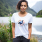 woman standing in front of a lake wearing a white t-shirt with a new zealand pukeko print