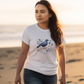 woman on the beach wearing a white t-shirt with a New Zealand Kokako bird print