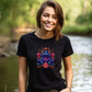 young woman beside a stream wearing a black t-shirt with a colorful floral frog print
