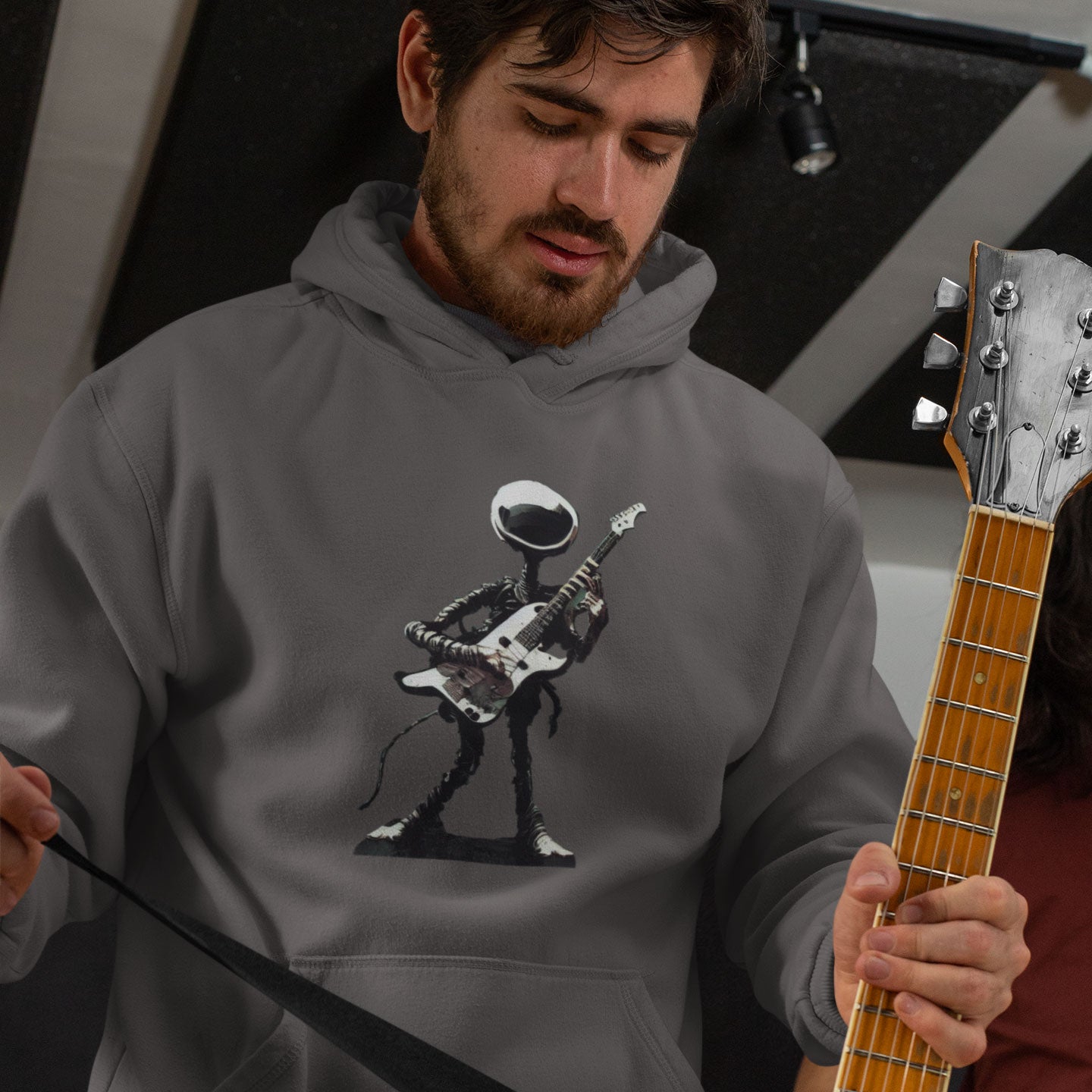 A guy holding a guitar wearing a grey hoodie with an alien guitarist print on the front